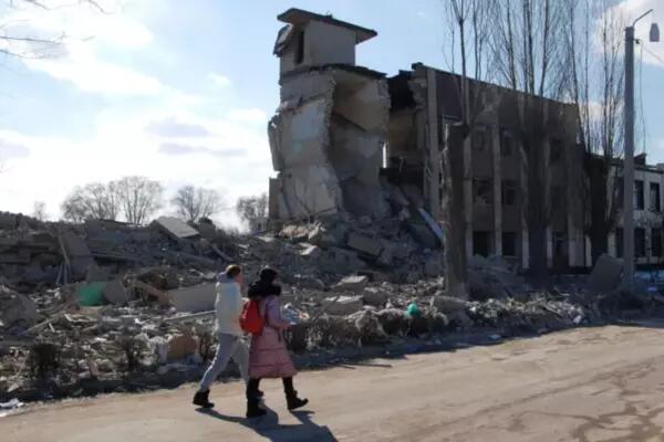 People walk past a school damaged by shelling, as Russia's invasion of Ukraine continues, in Kharkiv, Ukraine March 16, 2022 [Oleksandr Lapshyn/Reuters] (Reuters)