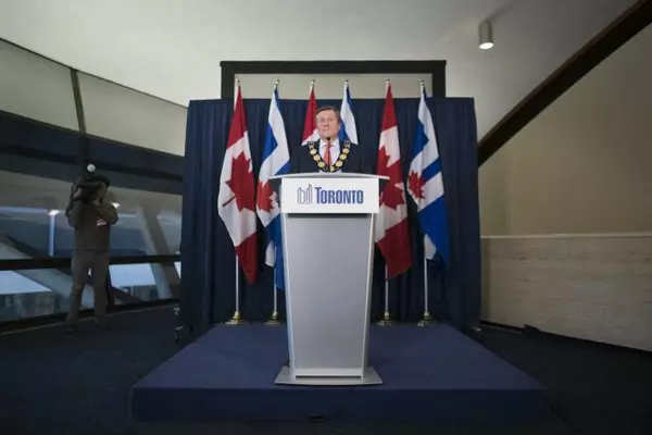 John Tory gives a speech at a Toronto logo podium, with Canadian and Ontario flag in the background.