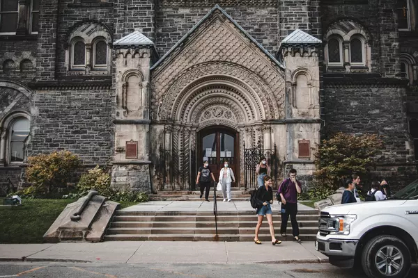 Students walk out of a stone building on the University of Toronto campus.
