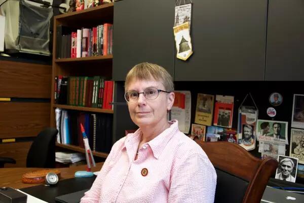 Lynne Viola sits in her office wearing a pink striped button up shirt and round glasses