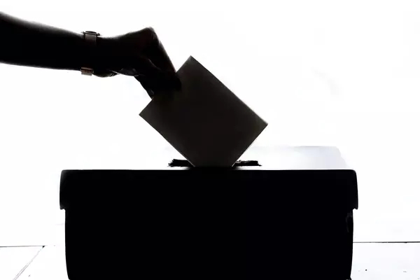 A silhouette of a person dropping a voting card in a ballot box.