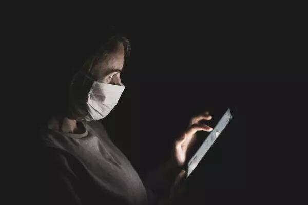 A masked woman swipes on her phone in the dark