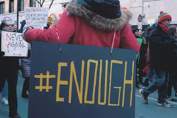 A woman at a protest holding a black sign that says #enough
