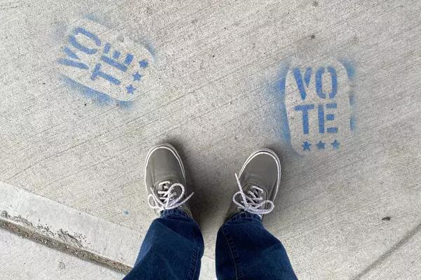 A person standing on concrete on which has been spray painted, in blue, the word vote
