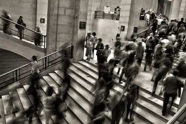 A black and white shot of a crowd moving through stone halls.