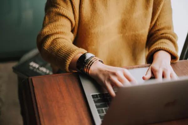A person in a yellow sweater typing on a laptop