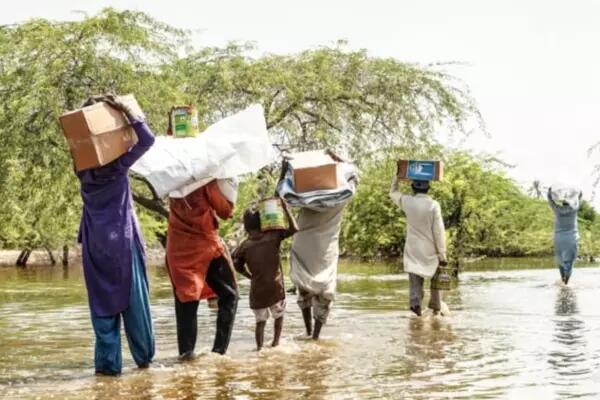 A group of Pakistanis carrying personal belongings tread in flood water