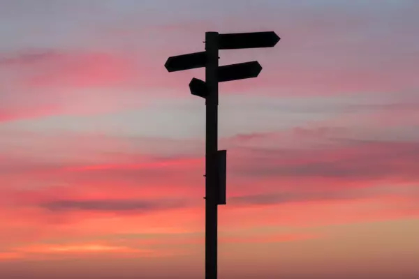 Four signposts pointing in different directions against a sunset