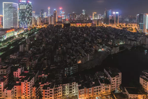 A large number of crumbling, dark, dormitory style apartment buildings for migrant workers are surrounded by tall, bright modern buildings in Guangzhou, China.