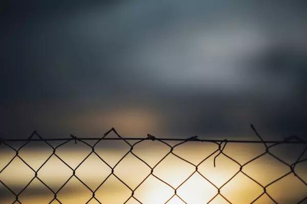 A fence with a bright light and grey clouds in the background