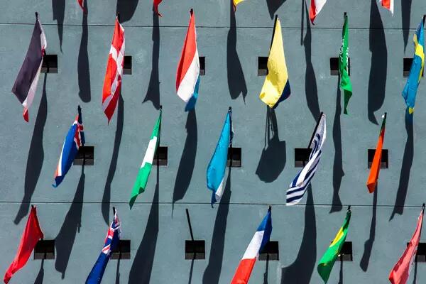 Aerial photo of many country flags blowing against a grey sidewalk