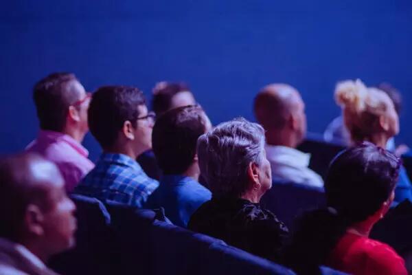 Rows of people sit in a dark auditorium