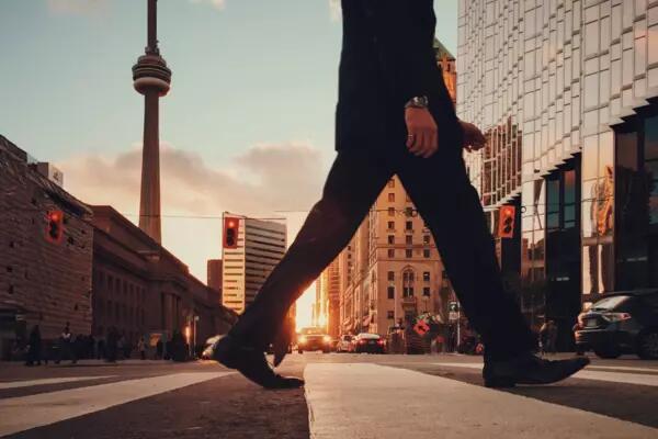 Shot of man's legs crossing the street by Union Station in Toronto. The CN tower is in the background.