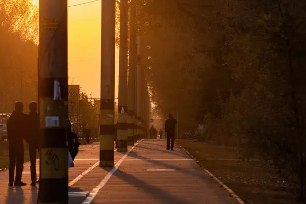 People wait at the train station, their silhouettes backlit by a golden sunset.