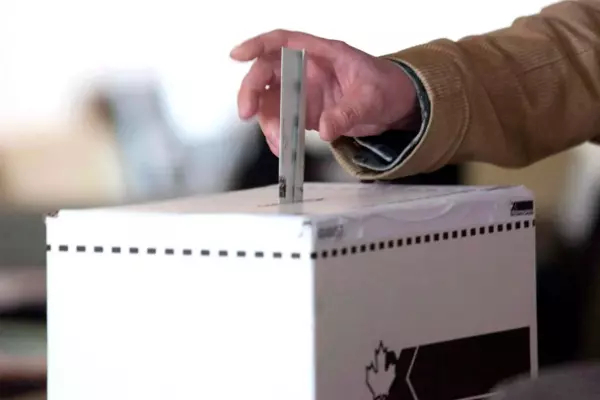 An individual drops their ballot into a white elections box