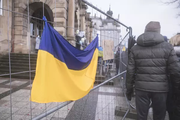 a wet ukrainian flag hanging on a fence, next to a protest in bielefeld, germany