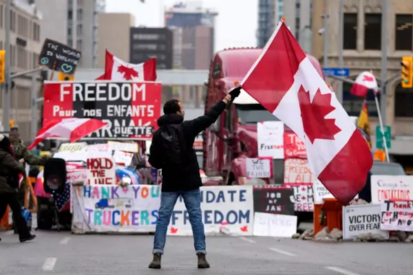 An individual waves a large Canadian flag in front of convoy protestors on the street