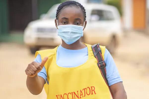 Health worker wearing a yellow vest bearing "Vaccinator" and a mask