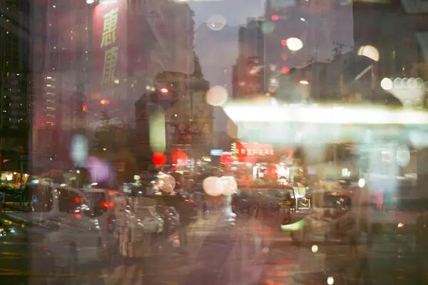 A Hong Kong street scene in the evening, with red lanterns, tall buildings in the background, and blurry lights from double exposure.