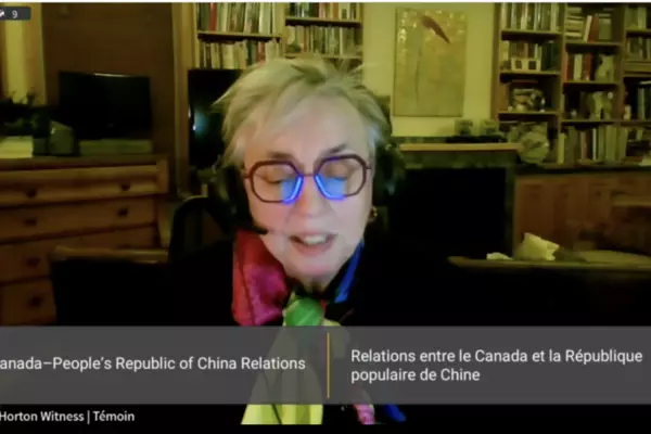 Woman sitting and wearing a microphone headset with the screen saying "Canada-People's Republic of China Relations" in English and French 