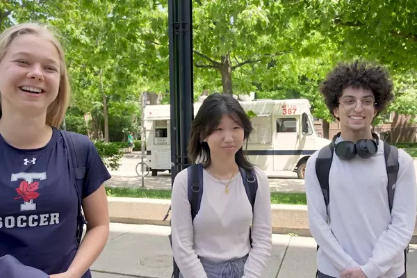 Three students in front of trees discussing their associations with capitalism.