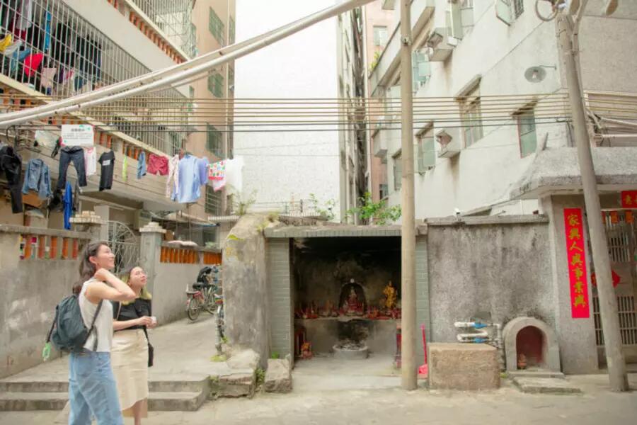 Woman walks through a street in Shenzhen looking up at hanging laundry and wires