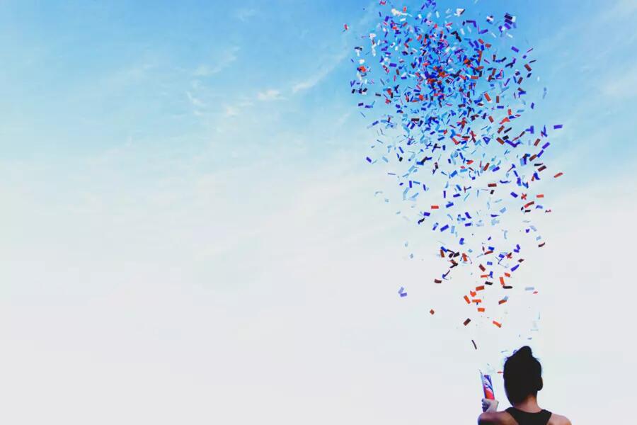 The back of a woman holding a confetti dispenser, and red white and blue confetti in the sky