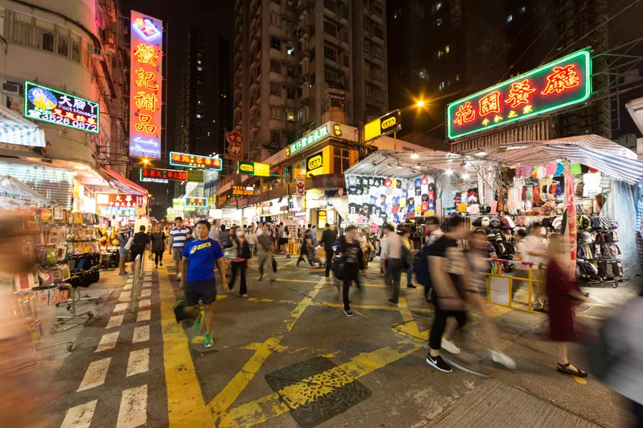 A crowded intersection in Hong Kong at night, lit up with street lights and signs.