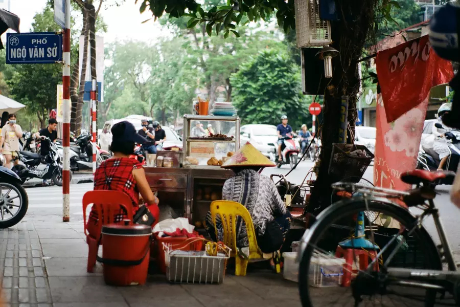 A street scene in Hanoi, including a food stall, bicycles, and street signs.
