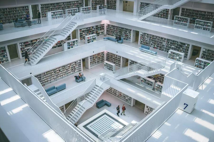 Multiple floors of a library with white floors, stairs and banisters and colourful books