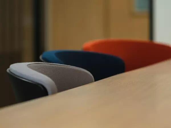 Rounded grey, blue and orange chairs lined up at a wood table