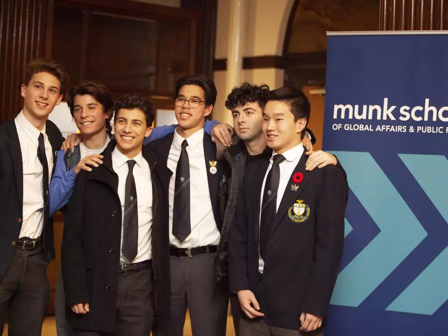 Five male students in blazers and ties pose in front of a Munk School banner