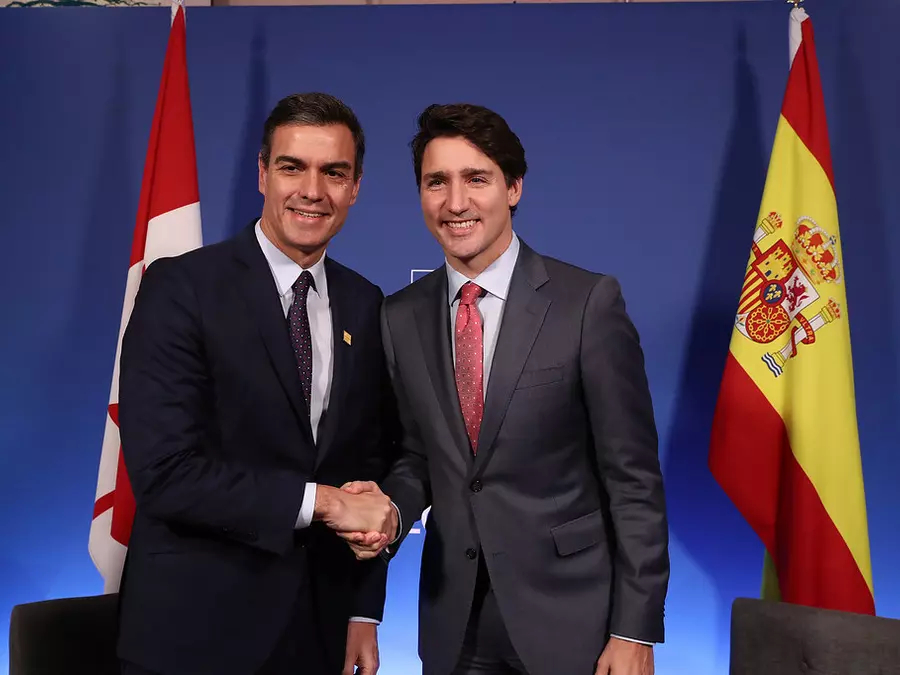 Pedro Sanchez and Justin Trudeau shake hands in front of a Canadian and Spanish flag