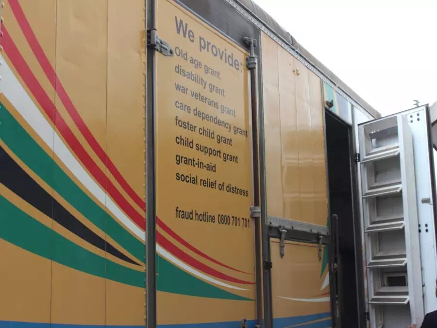A Truck with text on the side that provides various grants, such as child support, old age, disability, and veterans grants
