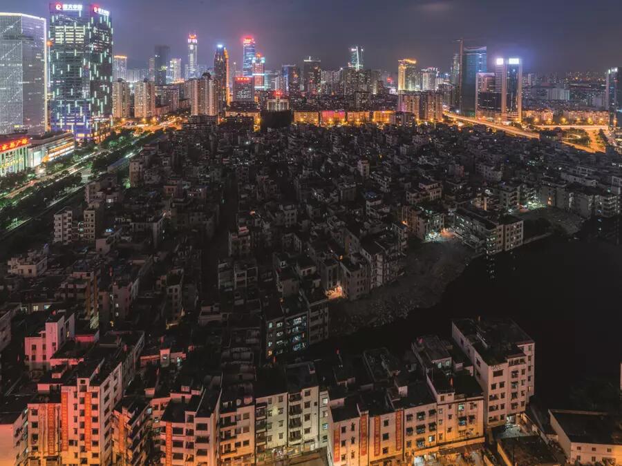 A large number of crumbling, dark, dormitory style apartment buildings for migrant workers are surrounded by tall, bright modern buildings in Guangzhou, China.