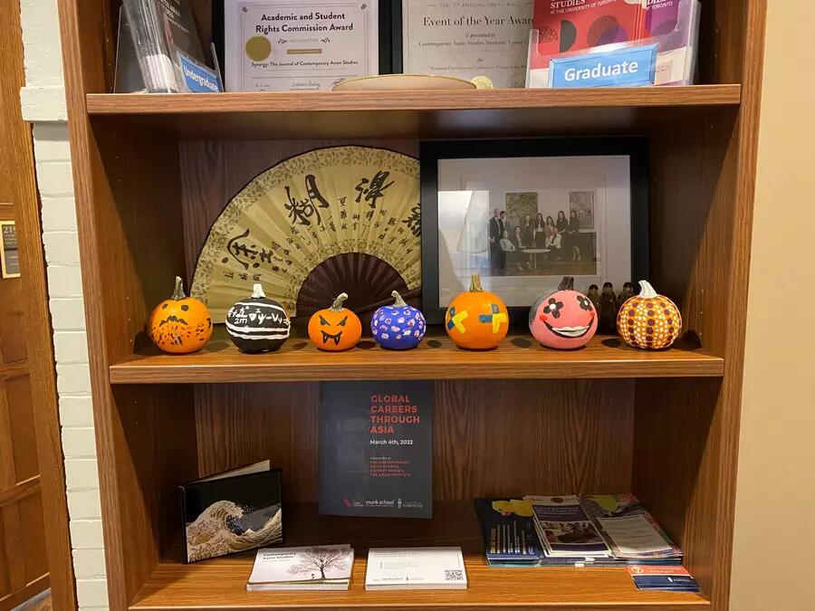 A collection of pumpkins are lined up on a wooden bookshelf.
