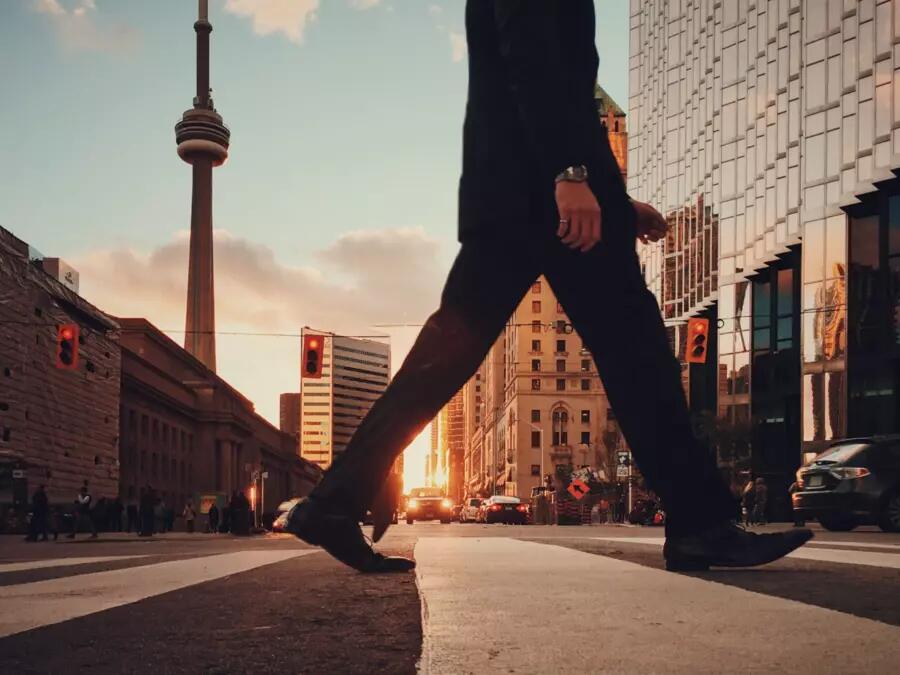 Shot of man's legs crossing the street by Union Station in Toronto. The CN tower is in the background.
