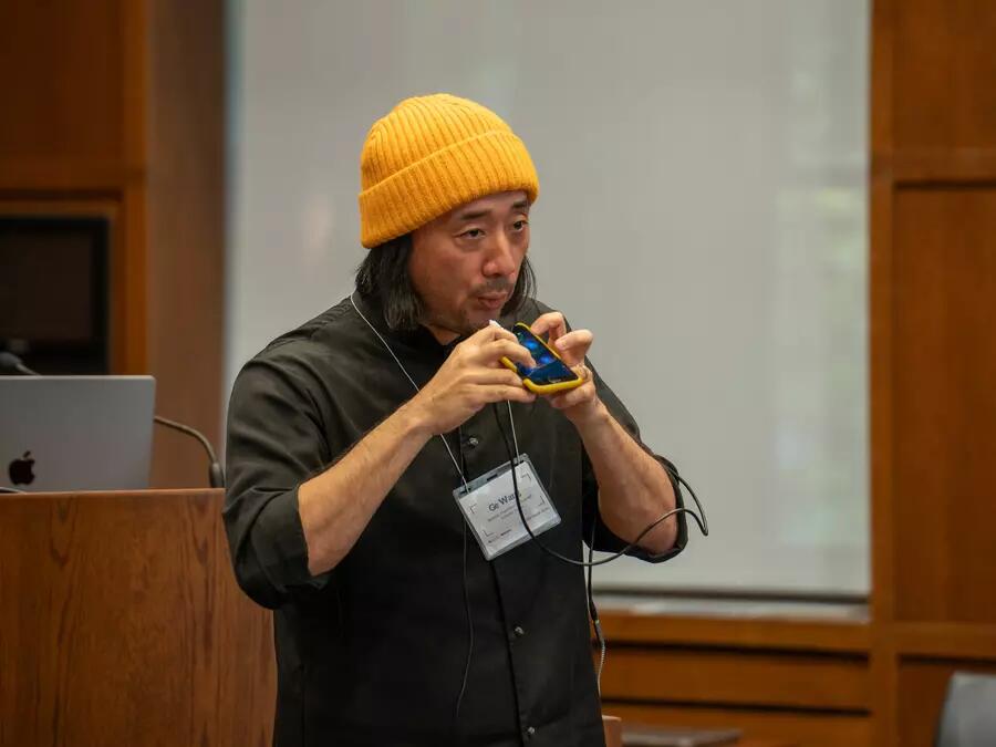 Professor Ge Wang wearing a yellow hat, and playing his instrument from his phone.