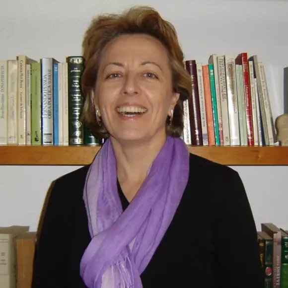 Picture of Marga Vicedo in front of bookshelf wearing black sweater and purple scarf. 