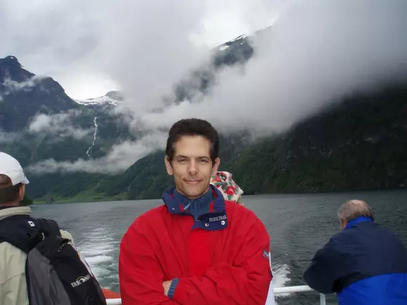 Picture of Mark Solovey standing on a boat in a red jacket. 
