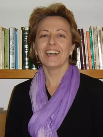 Picture of Marga Vicedo in front of bookshelf wearing black sweater and purple scarf. 