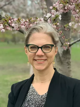 Picture of Pamela Klassen standing in front of a cherry blossom tree wearing a black blazer. 