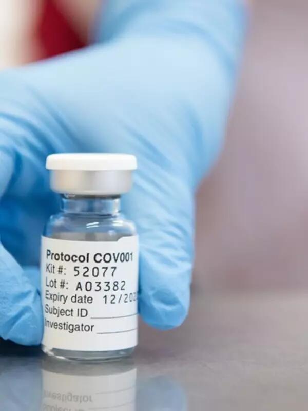 Blue gloved hand pushes forward a vial of the COVID vaccine