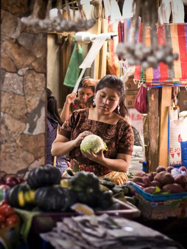 A Guatemalan woman standing in a fruit market, holding a head of lettuce.