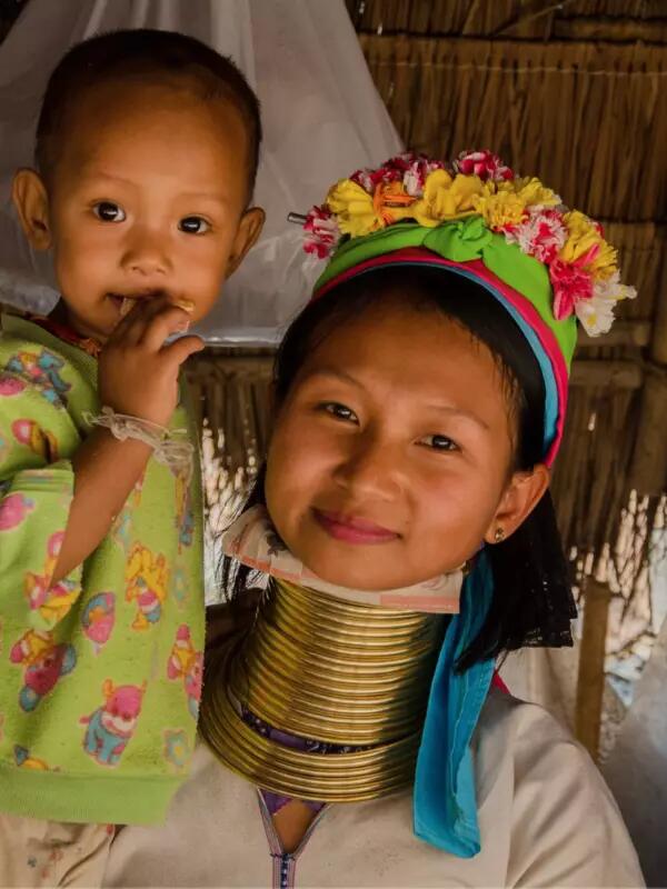 An image of a mother holding her child in Thailand. The mother wears a flowered headpiece with traditional gold neck rings
