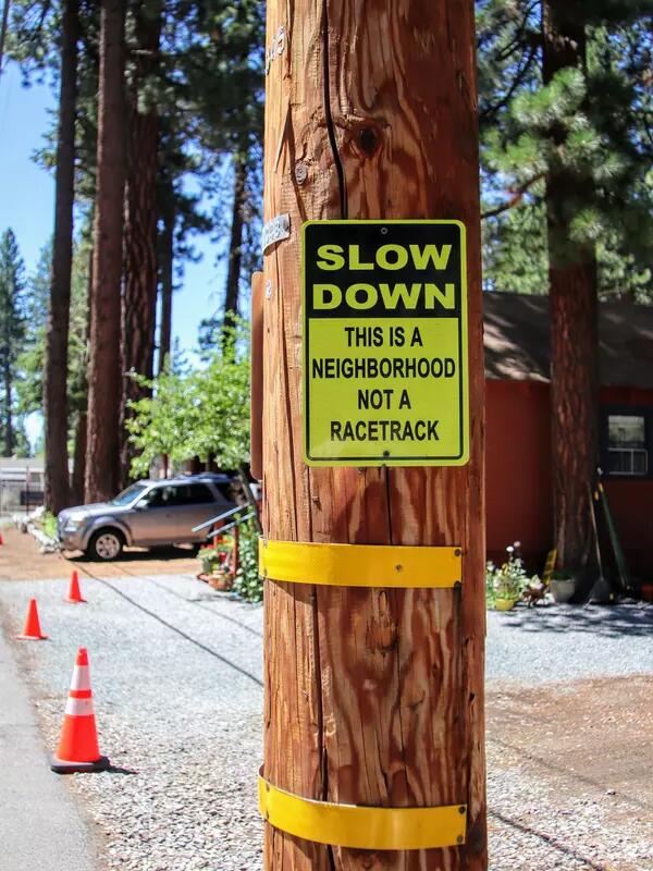 A wooden pole with a yellow traffic sign, reading "slow down, this is a neighbourhood not a racetrack"