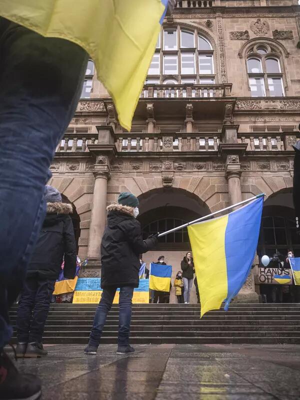 A protestor waves a Ukrainian flag in front of an ornate stone building.