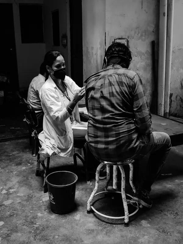 A black and white shot of a doctor giving a vaccine to a man in India.