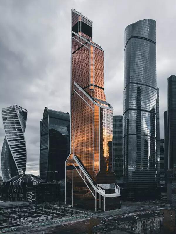 A copper coloured tower in Moscow is illuminated against other tall grey buildings.