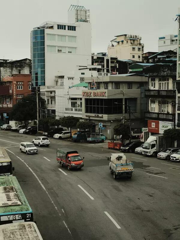 Cars drive on a city street lined with buildings in Myanmar.